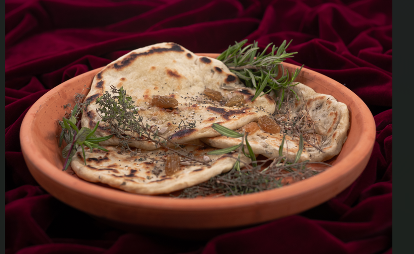 sur une assiette en terre cuite brune, avec 3 miches de pain plates, rondes et croustillantes