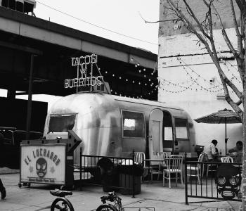 foto en blanco y negro de foodtruck metalizado con cartel de &quot;El luchador&quot; y otro que dice tacos y burritos 