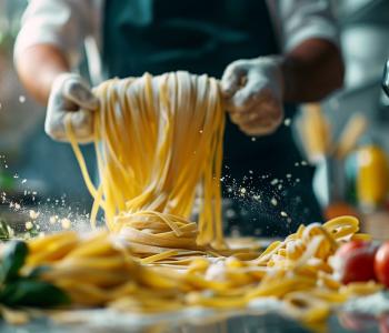 Foto de manos de cocinero enroscando espaguetis con harina sobre una mesa con tomates y albahaca