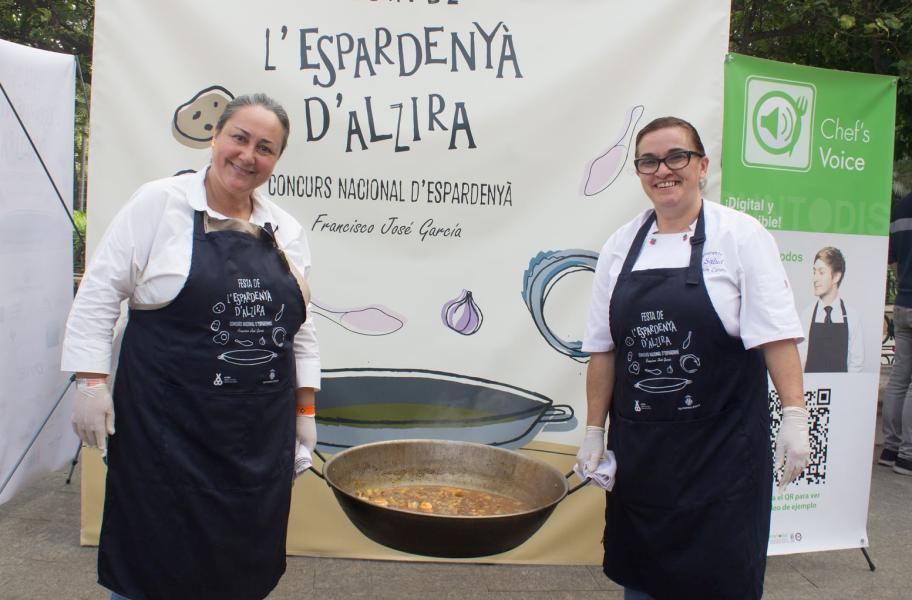 Concurso de la Espadenya 2 mujeres sonríen mientras sujetan un caldero con el guiso de la espadeñá